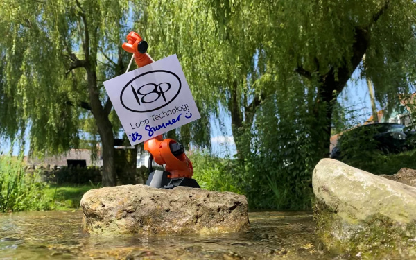 An image of a small Kuka robot holding a sign next to a river.